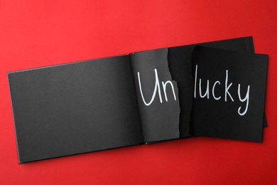 Torn word UNLUCKY written in notebook on red background, top view