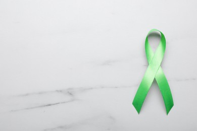 World Mental Health Day. Green ribbon on white marble table, top view with space for text