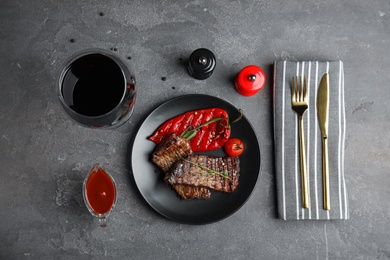 Photo of Grilled meat served with garnish and sauce on grey table, flat lay