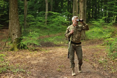 Photo of Man with hunting rifle looking through binoculars in forest. Space for text