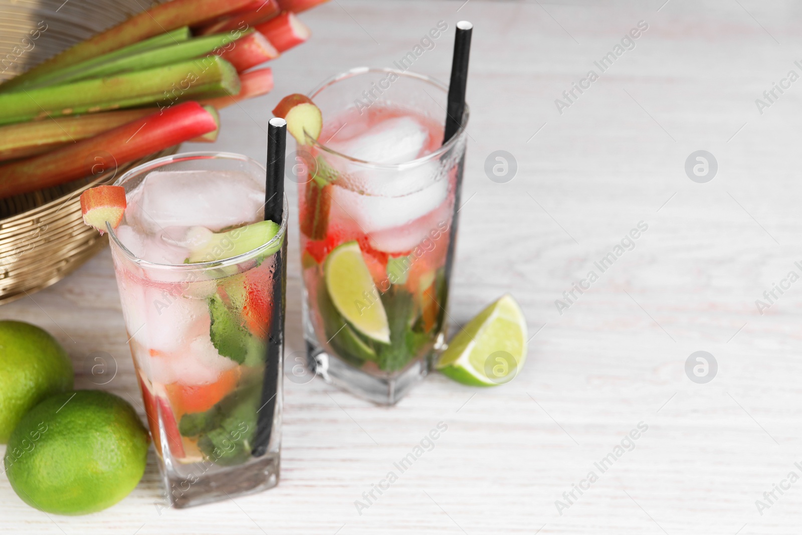 Photo of Tasty rhubarb cocktail with lime on white wooden table, space for text