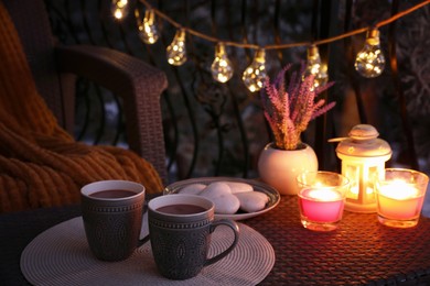 Cups with tasty cocoa on rattan table at balcony in evening