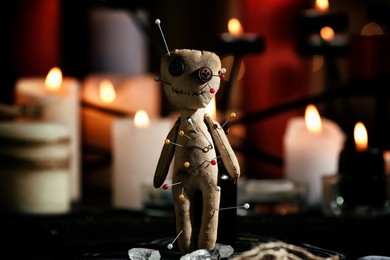 Photo of Voodoo doll pierced with pins on table in dark room. Curse ceremony