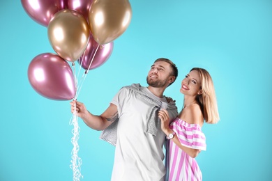 Young couple with air balloons on color background