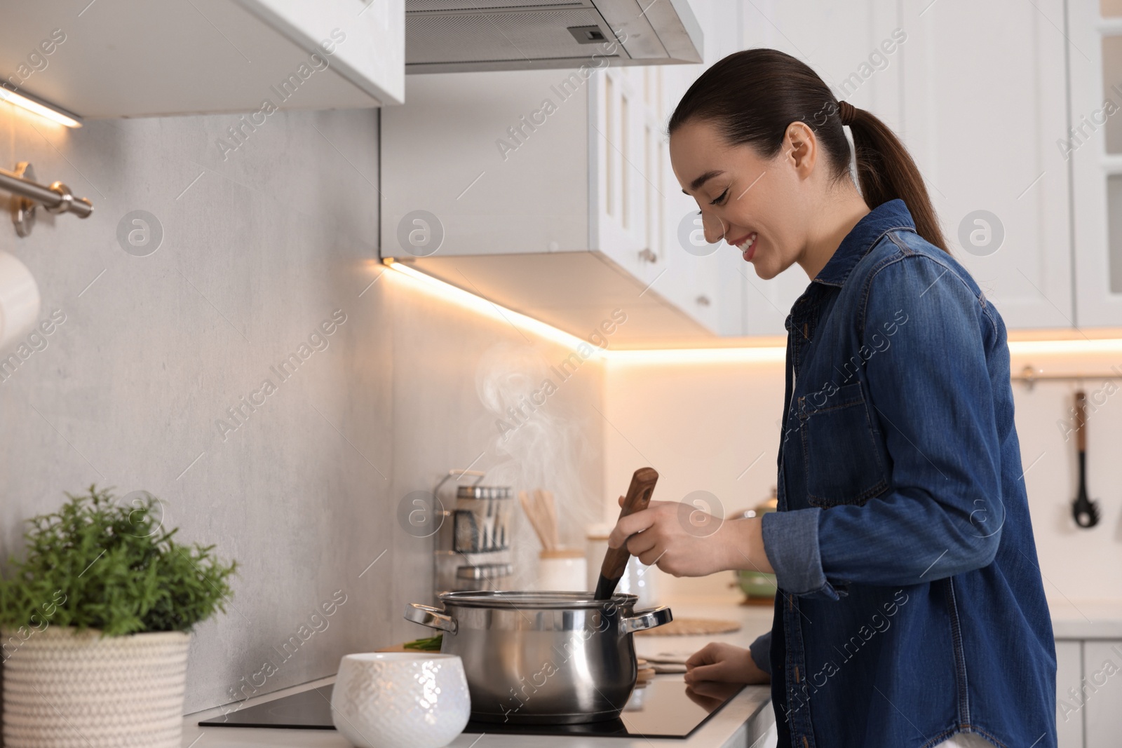 Photo of Smiling woman with ladle cooking soup in kitchen