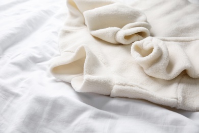 Photo of Warm fleece sweater on white crumpled fabric, closeup