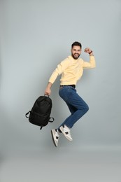 Emotional man with stylish backpack jumping on light grey background