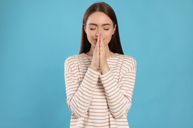 Woman with clasped hands praying on turquoise background