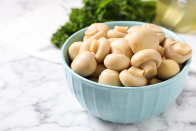 Tasty marinated mushrooms in bowl on white marble table, closeup