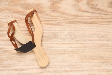 Photo of Slingshot with leather pouch on wooden background, top view. Space for text