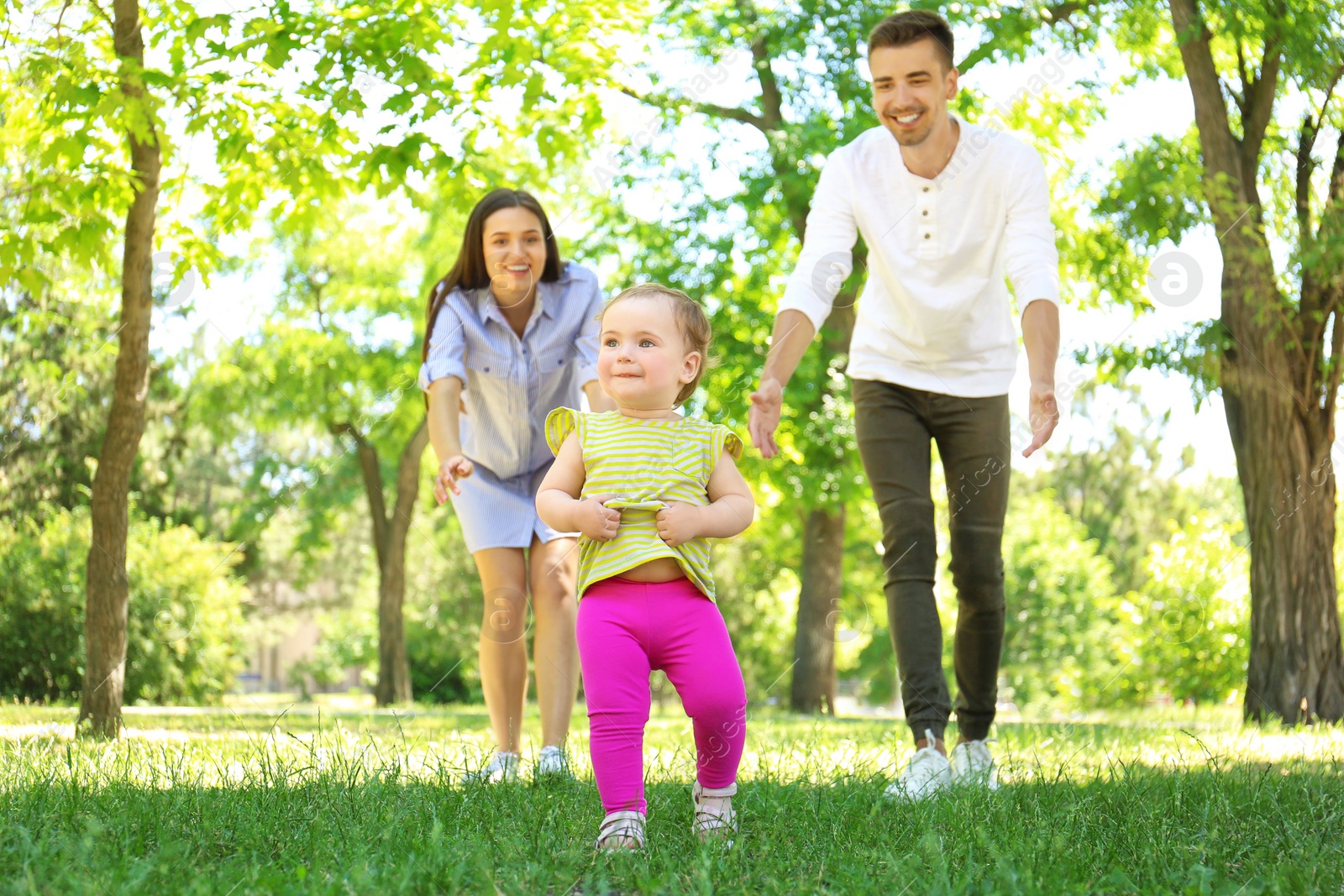 Photo of Parents supporting their baby daughter while she learning to walk outdoors