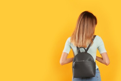 Photo of Woman with backpack on yellow background, back view. Space for text