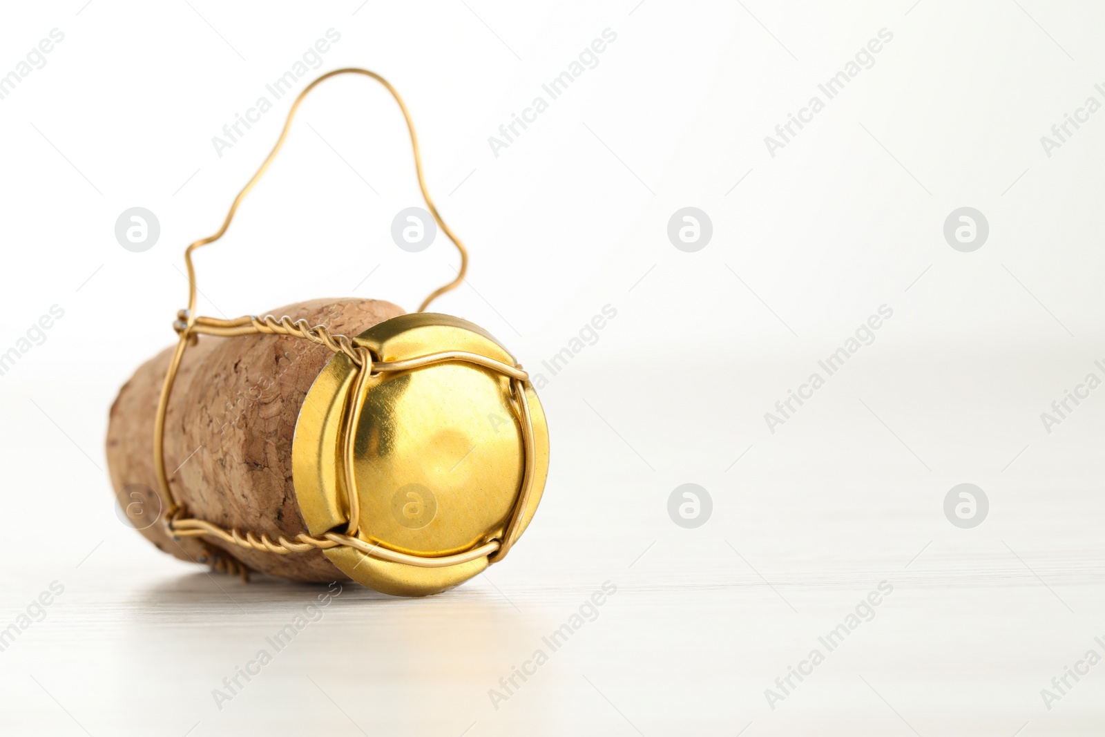 Photo of Cork of sparkling wine and muselet cap on white wooden table, closeup. Space for text