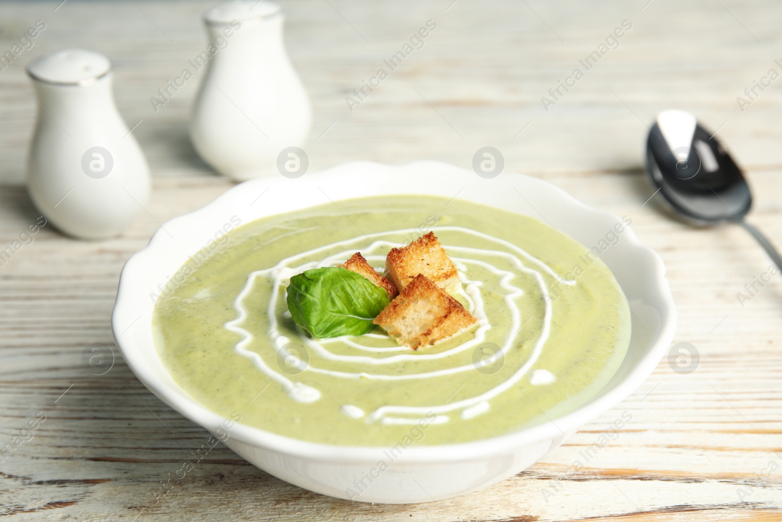 Photo of Delicious broccoli cream soup with croutons served on white wooden table