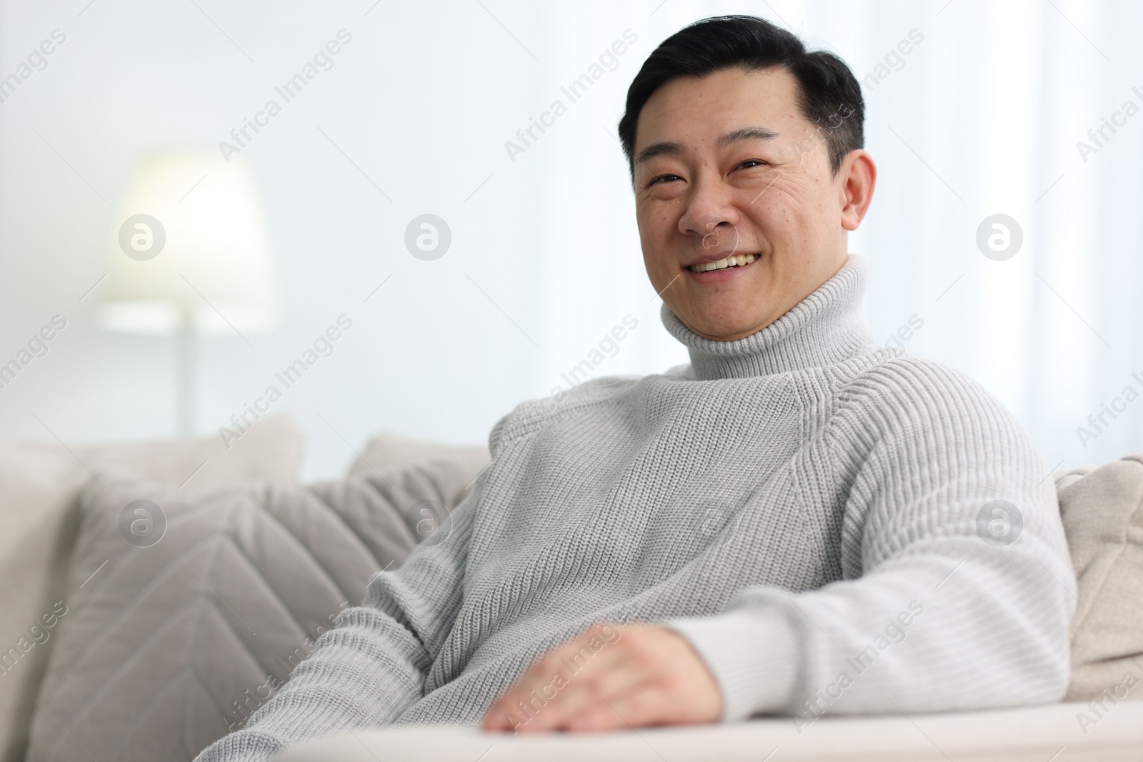 Photo of Portrait of smiling man on sofa indoors. Space for text