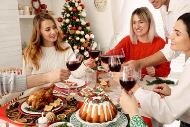 Photo of Happy family with their friends clinking glasses at festive dinner indoors. Christmas Eve celebration