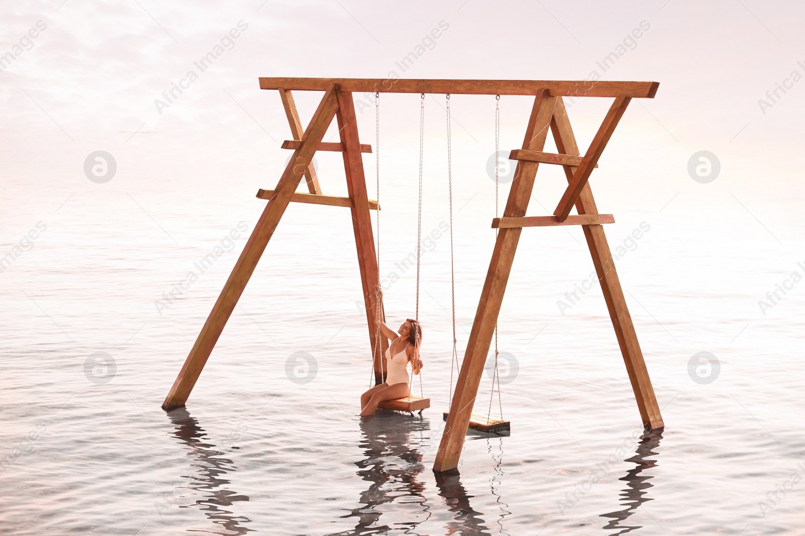 Photo of Young woman enjoying sunrise on swing over water