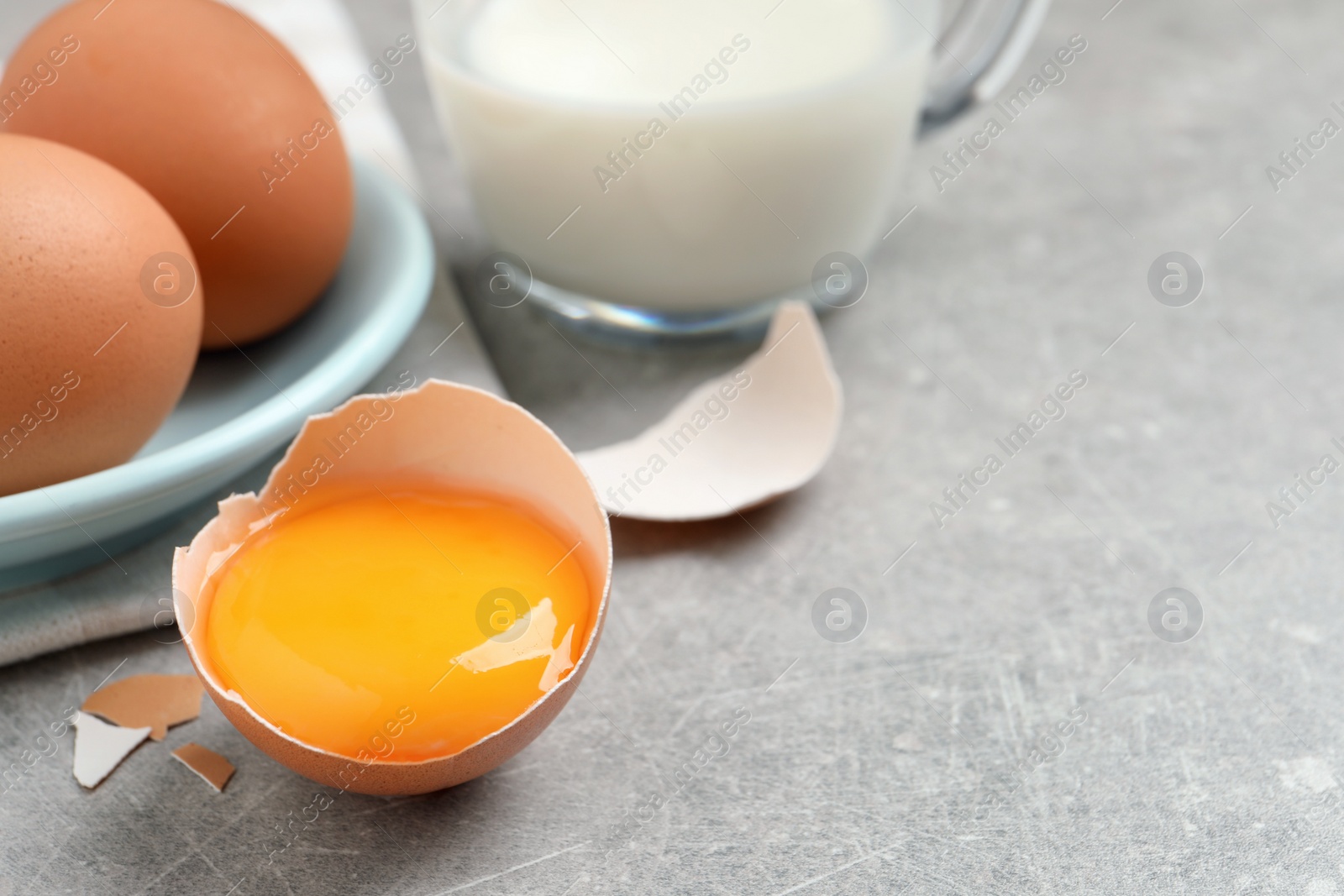 Photo of Raw chicken eggs and shell with yolk on light grey table, closeup. Space for text