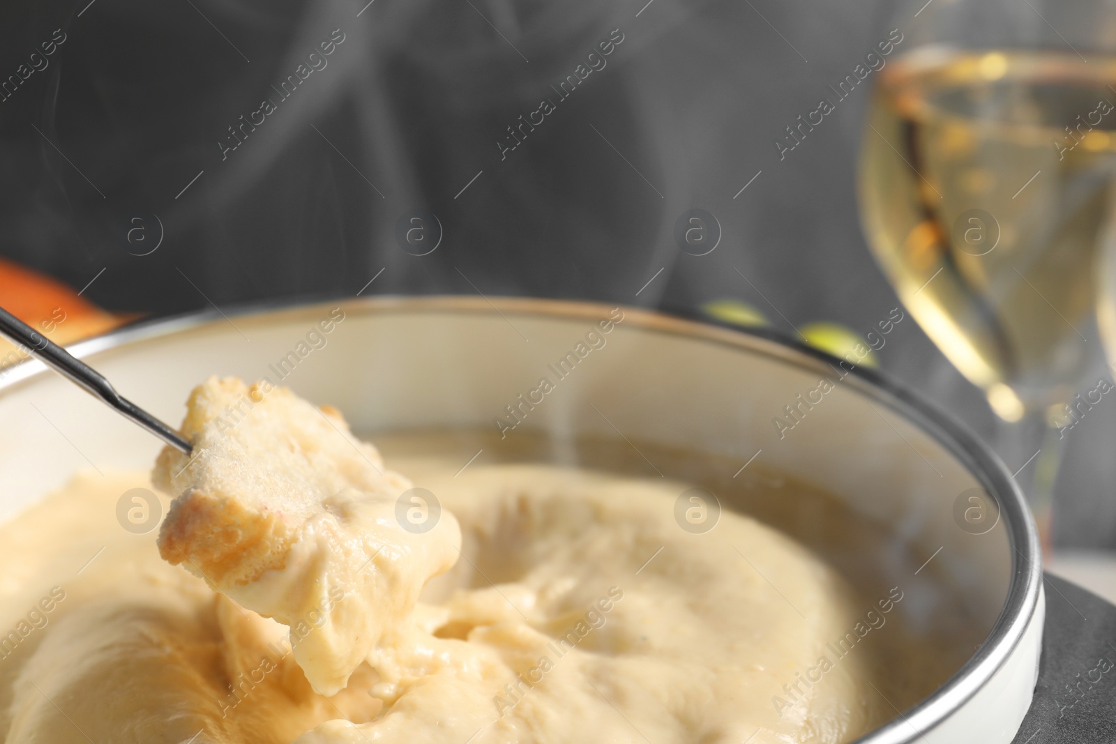 Photo of Dipping piece of bread into fondue pot with melted cheese on grey background, closeup