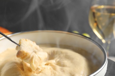 Dipping piece of bread into fondue pot with melted cheese on grey background, closeup