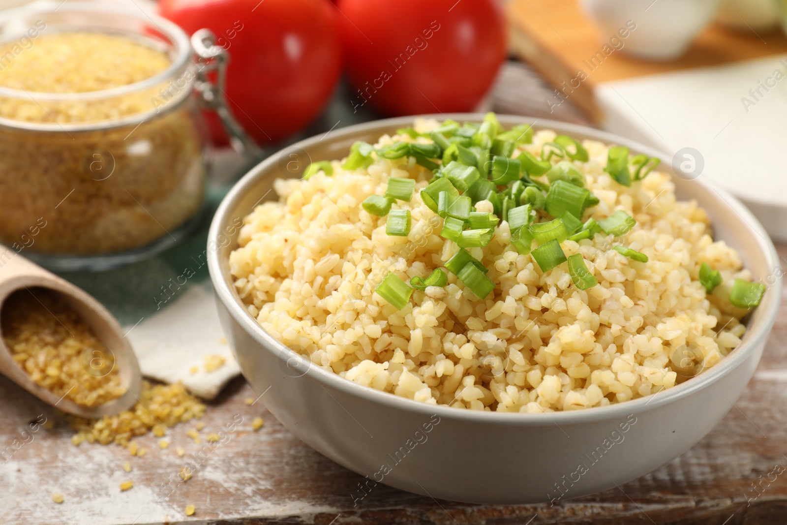 Photo of Delicious bulgur with green onion on wooden table, closeup