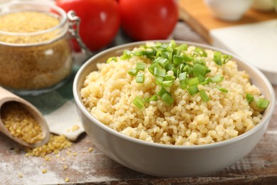 Photo of Delicious bulgur with green onion on wooden table, closeup