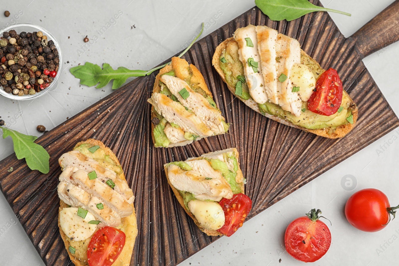 Photo of Board with delicious chicken bruschettas on light grey table, flat lay