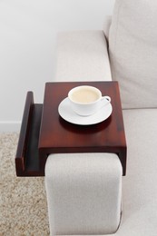 Photo of Cup of coffee on sofa with wooden armrest table indoors. Interior element