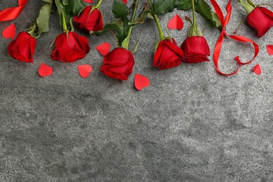 Flat lay composition with beautiful red roses and paper hearts on grey background, space for text. Valentine's Day celebration