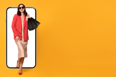 Online shopping. Happy woman with paper bags walking out from smartphone on orange background, space for text