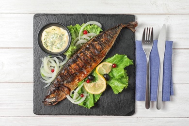 Photo of Slate plate with delicious grilled fish and sauce on wooden table, top view