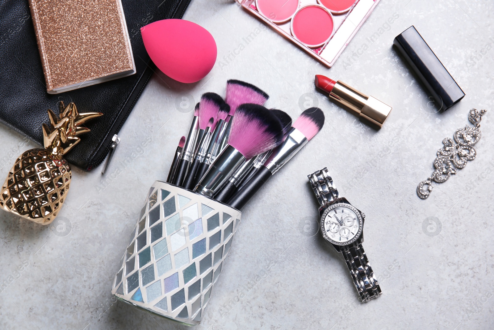 Photo of Holder with professional brushes, makeup products and accessories on light background, top view