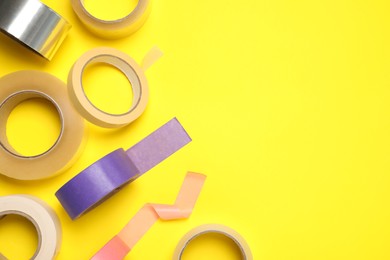 Photo of Many rolls of adhesive tape on yellow background, flat lay. Space for text
