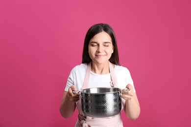 Happy young woman with cooking pot on pink background