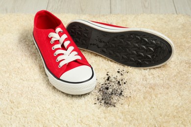 Red sneakers and mud on beige carpet, closeup