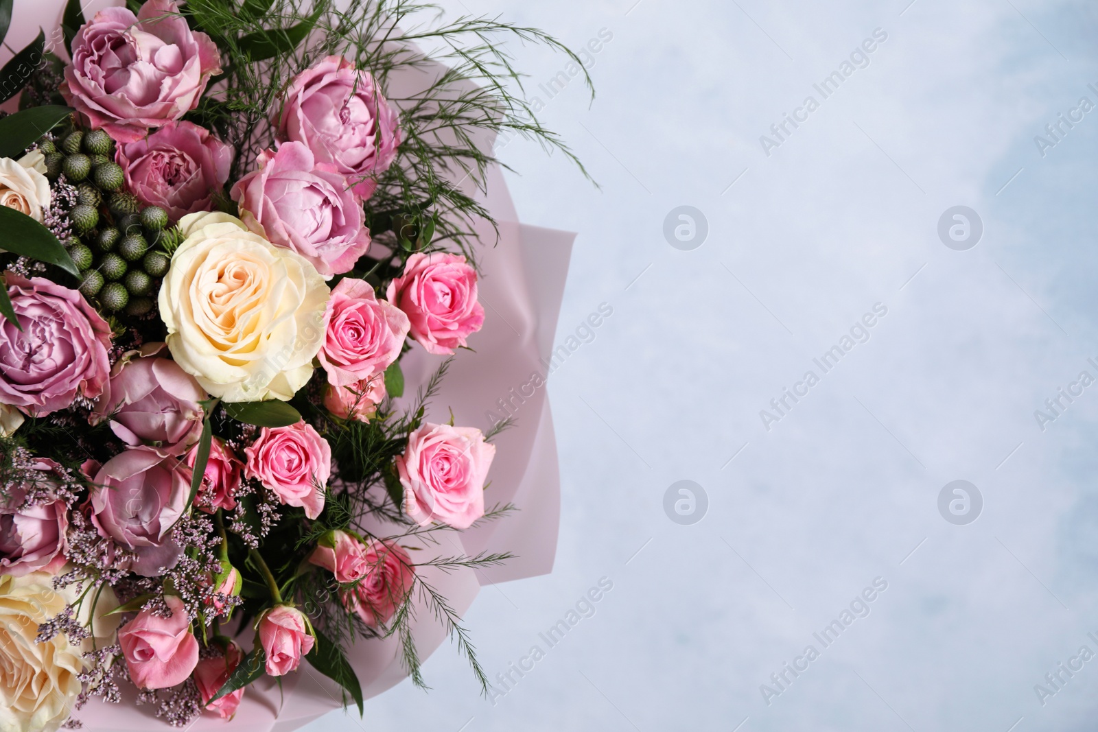 Photo of Beautiful bouquet with roses on light blue background, closeup. Space for text