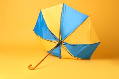 Photo of Broken bright umbrella with wooden handle on yellow background