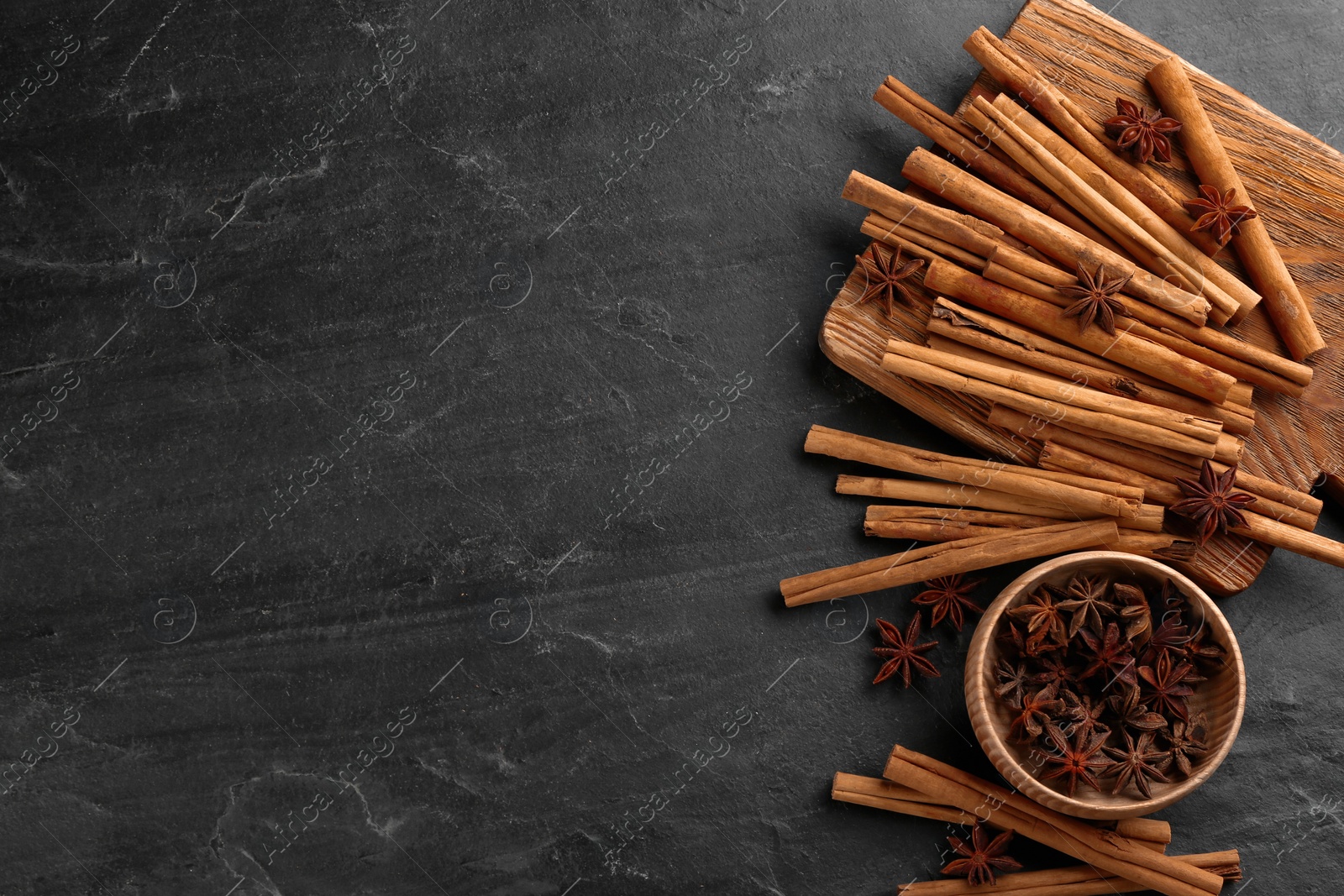 Photo of Aromatic cinnamon sticks and anise on black table, flat lay. Space for text