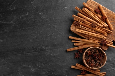 Aromatic cinnamon sticks and anise on black table, flat lay. Space for text