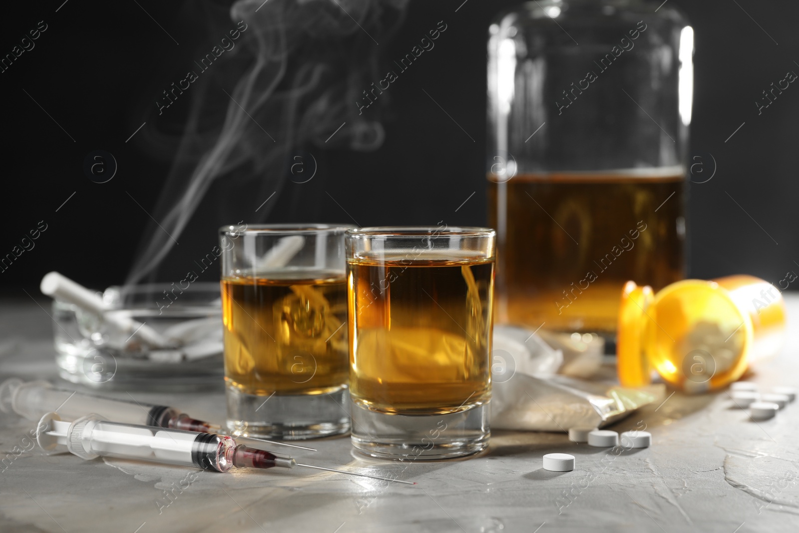 Photo of Alcohol and drug addiction. Whiskey in glasses, syringes, pills and cocaine on grey table