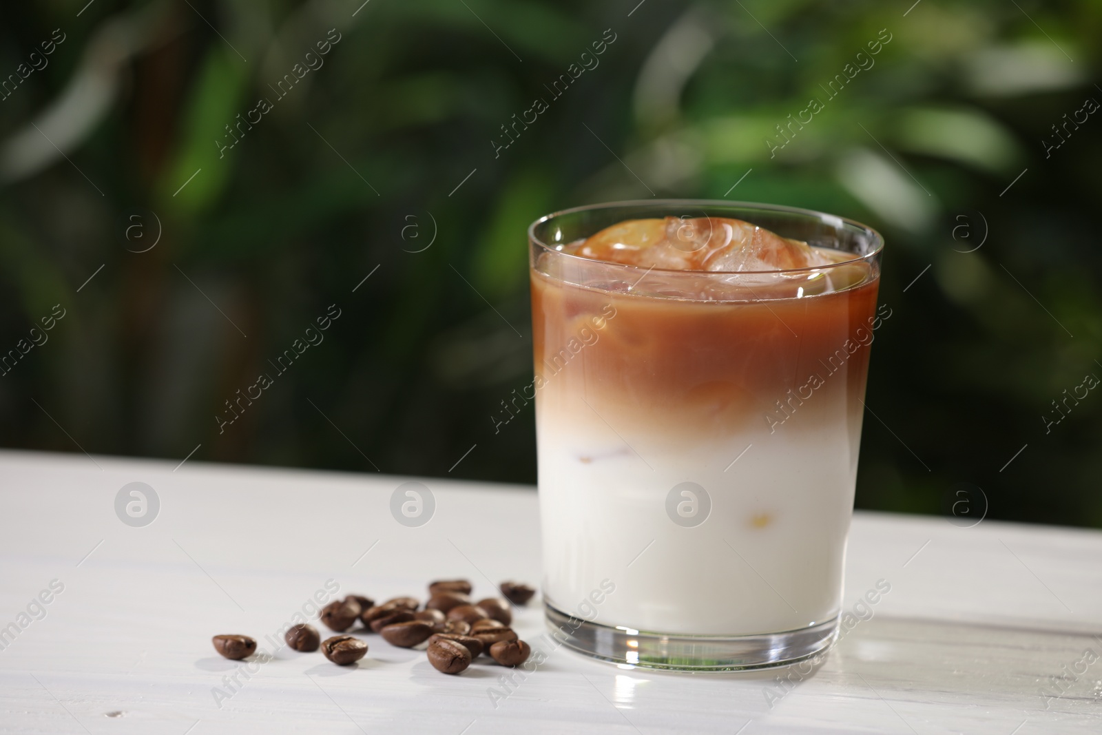 Photo of Glass of iced coffee and beans on white wooden table outdoors. Space for text