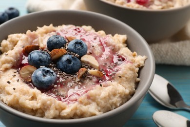 Photo of Tasty oatmeal porridge with toppings on light blue wooden table, closeup