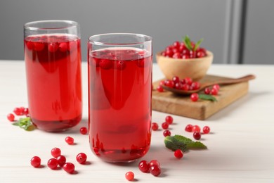 Tasty cranberry juice in glasses and fresh berries on white wooden table, closeup