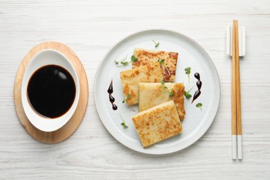 Photo of Delicious turnip cake and soy sauce served on white wooden table, flat lay