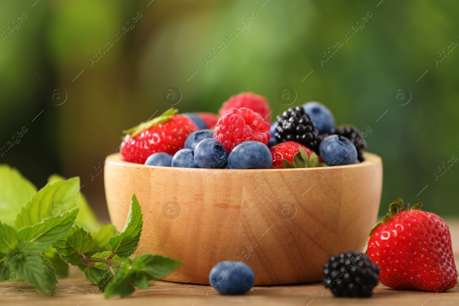 Photo of Bowl with different fresh ripe berries and mint on table outdoors, closeup