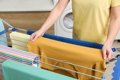 Photo of Young woman hanging clean laundry on drying rack in bathroom, closeup