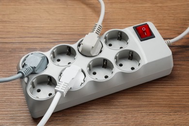 Photo of Power strip with extension cord on wooden floor, closeup. Electrician's equipment