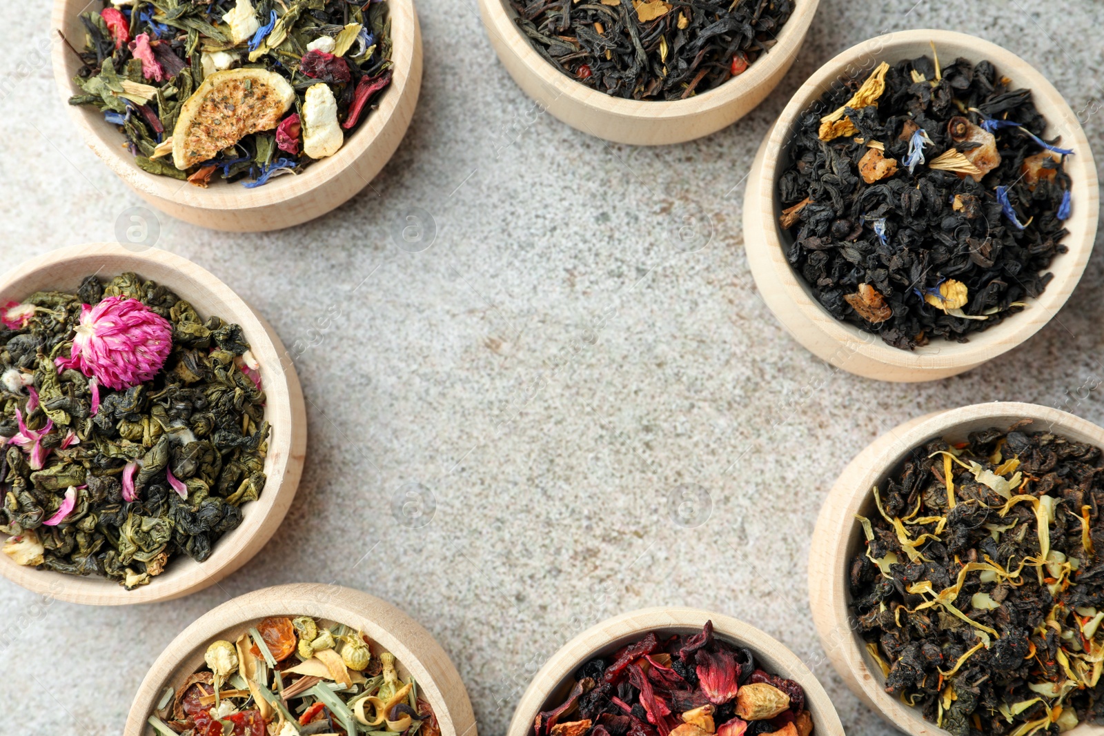 Photo of Different kinds of dry herbal tea in wooden bowls on light grey table, flat lay. Space for text