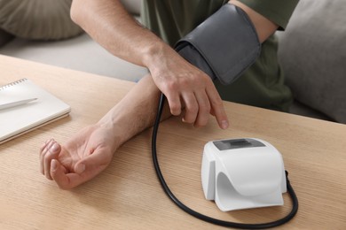 Photo of Man measuring blood pressure at wooden table in room, closeup