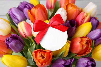 Bouquet of beautiful colorful tulips with blank card on white wooden background, closeup. Birthday celebration